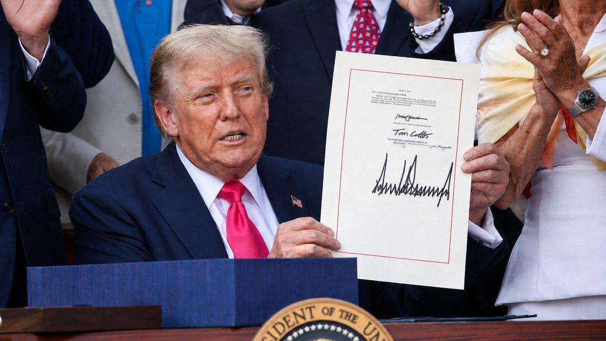 Hombre con traje y corbata rosa sosteniendo un documento firmado junto al podio con sello presidencial