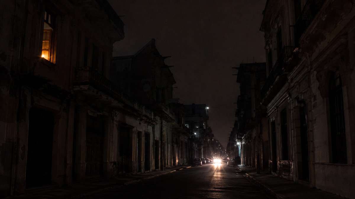 Calle oscura y desierta de edificios antiguos con faros de un coche al fondo y una ventana iluminada Calle oscura y desierta de edificios antiguos con faros de un coche al fondo y una ventana iluminada