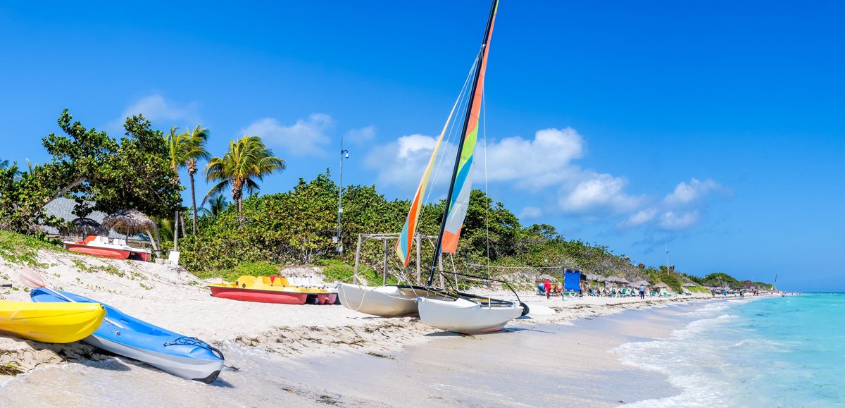 Playa caribeña con catamarán de vela colorida, kayaks en la arena y palmeras junto al mar turquesa Playa caribeña con catamarán de vela colorida, kayaks en la arena y palmeras junto al mar turquesa